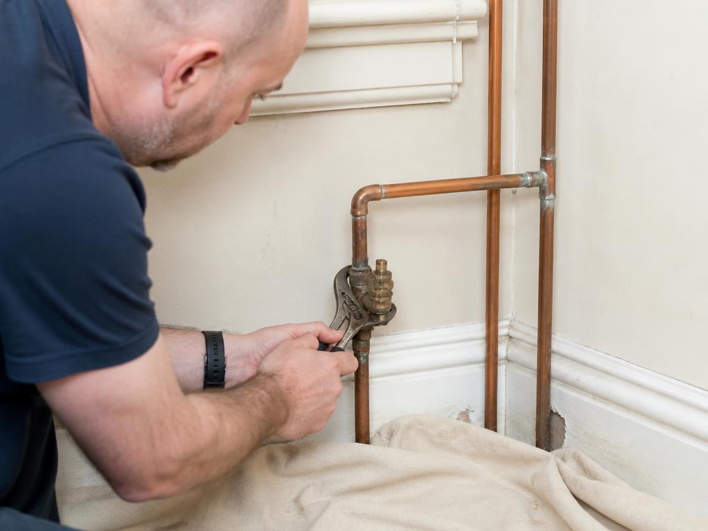 Plumber removing an old brass stop tap from copper pipework with a spanner
